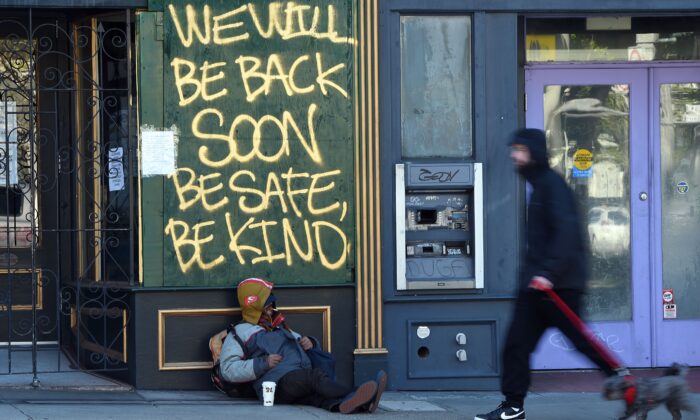 A man walks his dog past a homeless man sleeping under a message painted on a boarded up shop in San Francisco, Calif., on April 1, 2020. (Josh Edelson/AFP via Getty Images)