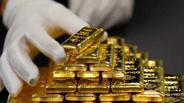 A gloved hand stacks bars of gold into a pyramid. (Leonhard Foeger/Reuters)