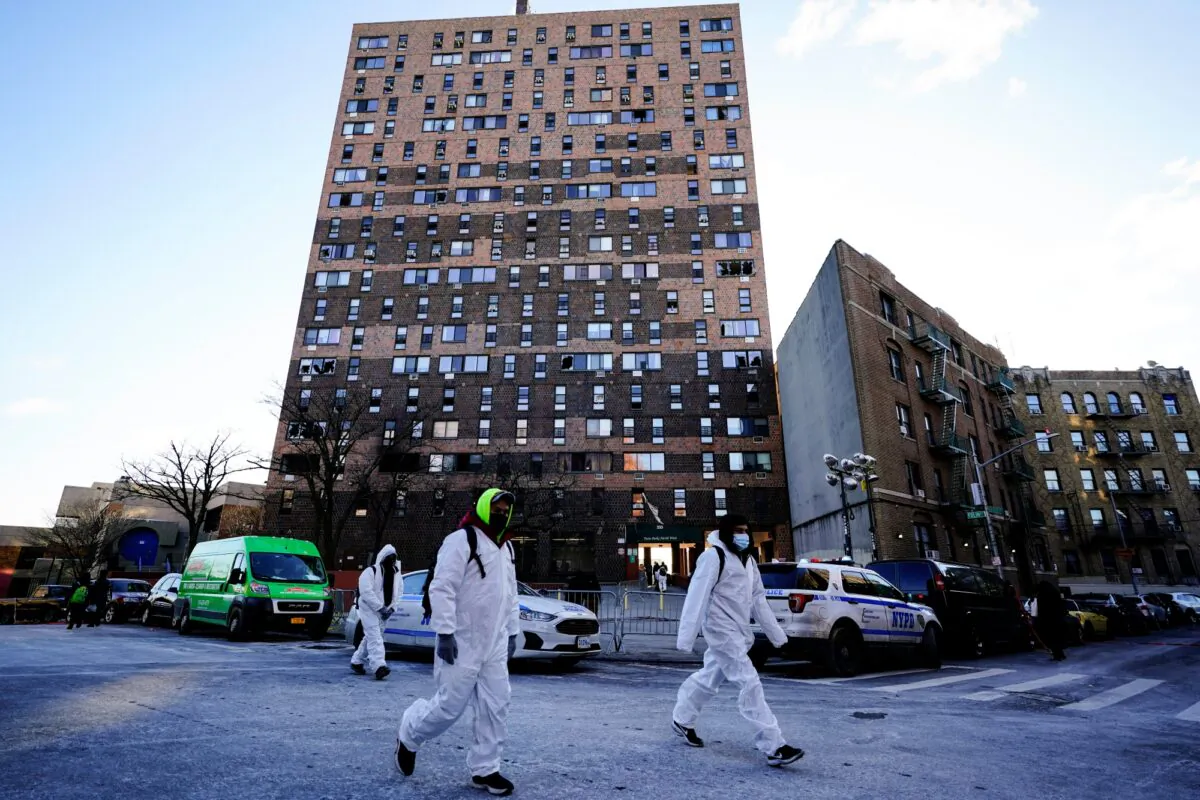 Workers in protective clothing walk from an apartment building in the Bronx borough of New York, on Jan. 11, 2022. (Matt Rourke/AP Photo)