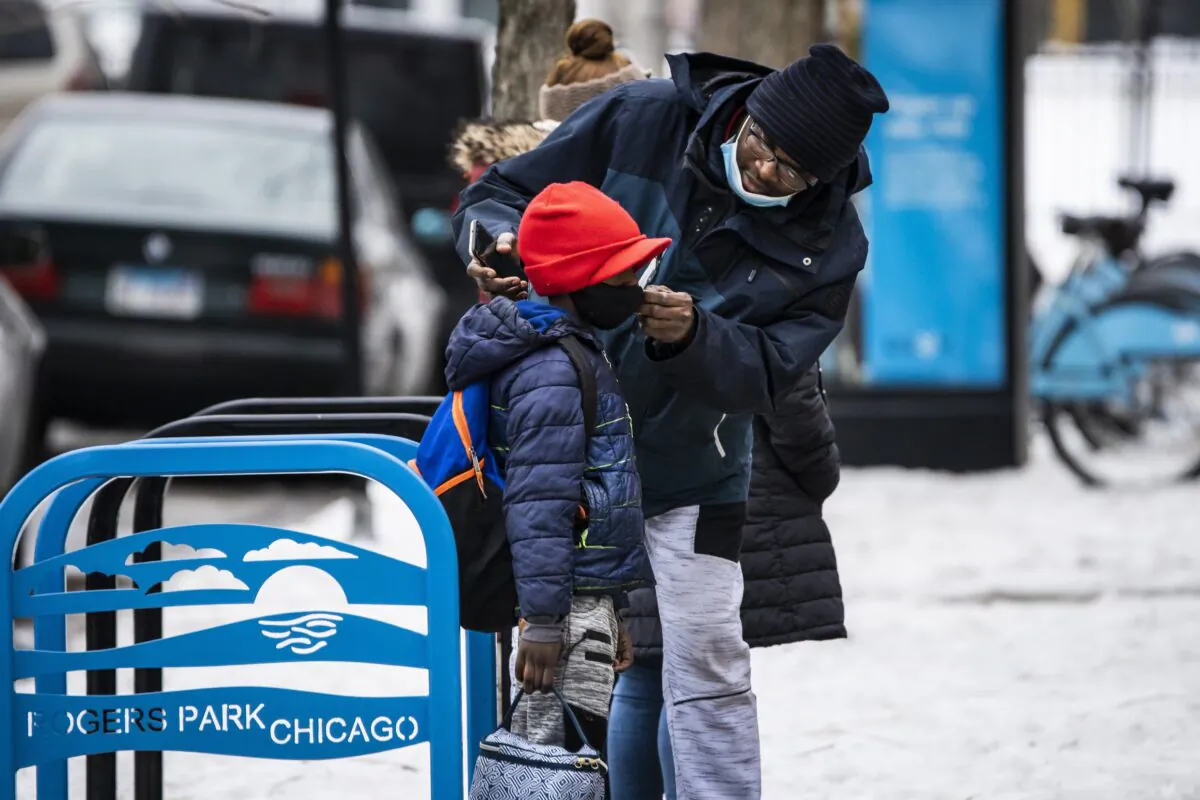 A man adjusts a boy's mask as they arrive at a school in Chicago, Ill., on Jan. 12, 2022. (Ashlee Rezin /Chicago Sun-Times via AP)