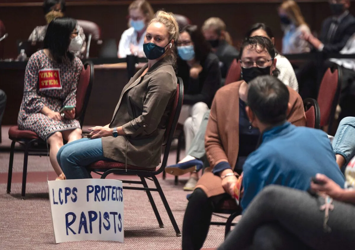 A woman sits with her sign during a Loudoun County Public Schools (LCPS) board meeting in Ashburn, Virginia on Oct. 12, 2021. (ANDREW CABALLERO-REYNOLDS/AFP via Getty Images)