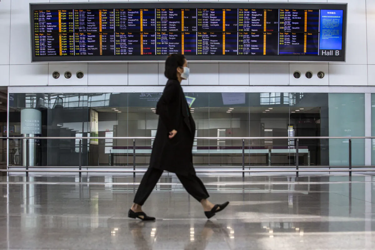 A women walks past a flight information board at Hong Kong International Airport, on Aug. 11, 2021. (Isaac Lawrence/AFP via Getty Images)