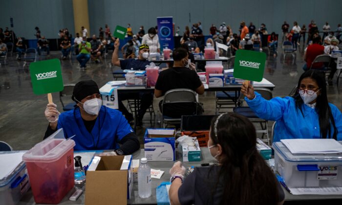 Health workers raise green signs to let know they are available to vaccinate people at the Puerto Rico Convention Center in San Juan, Puerto Rico, on March 31, 2021. (Ricardo Arduengo/AFP via Getty Images)