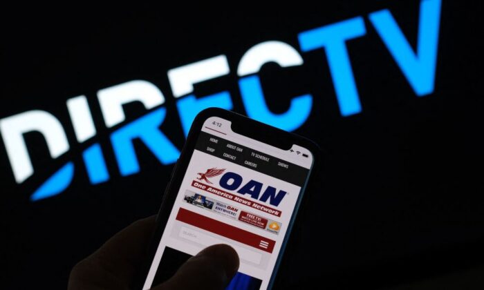 This illustration photo shows a person reading the One America Network website on a smartphone in front of a DirecTV logo in Los Angeles, Jan. 14, 2022. (Chris Delmas/AFP via Getty Images)