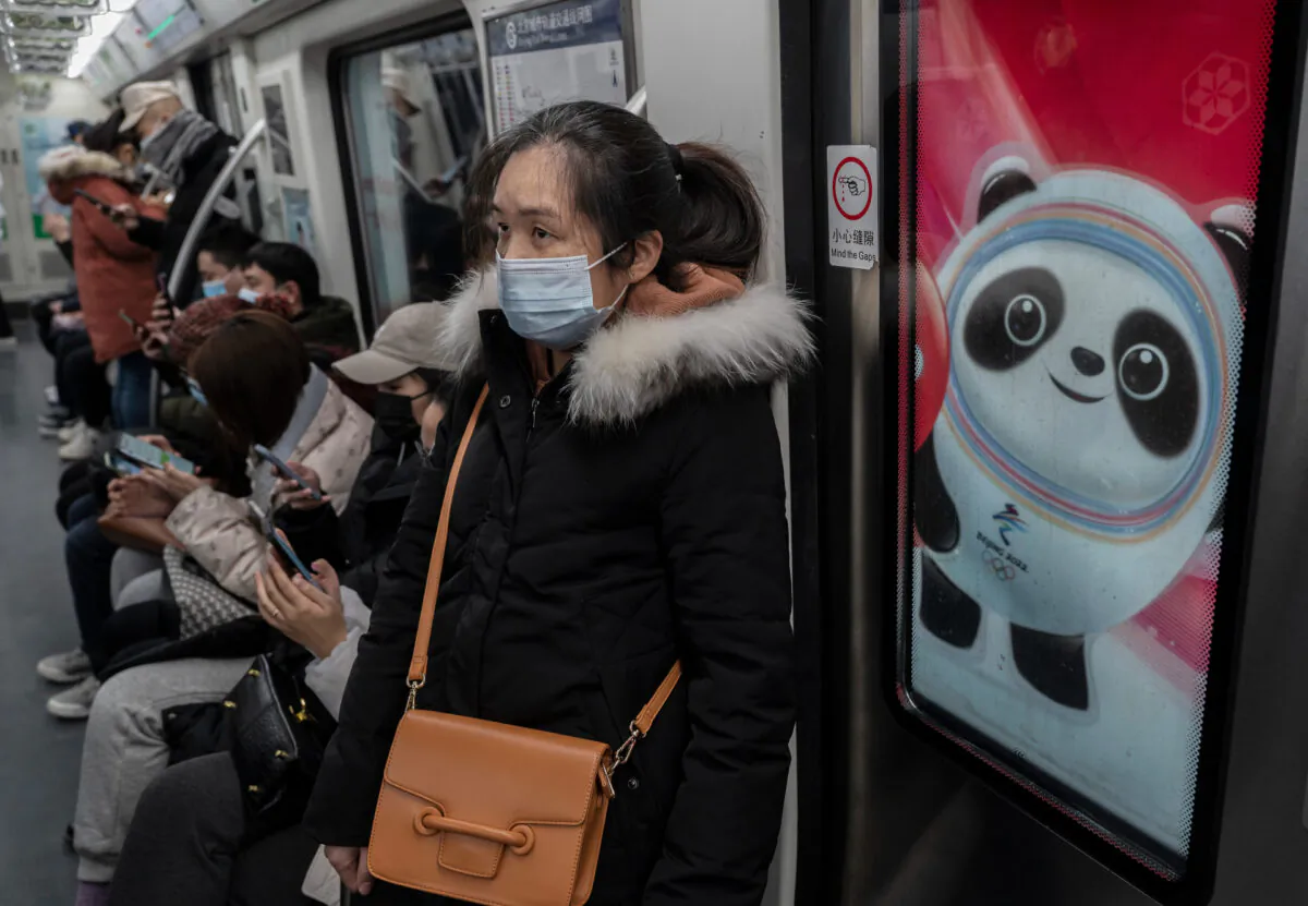A woman people ride on a metro car next to a logo for Beijing 2022 Winter Olympics mascot Bing Dwen Dwen during rush hour in Beijing on Jan. 13, 2022. (Kevin Frayer/Getty Images)