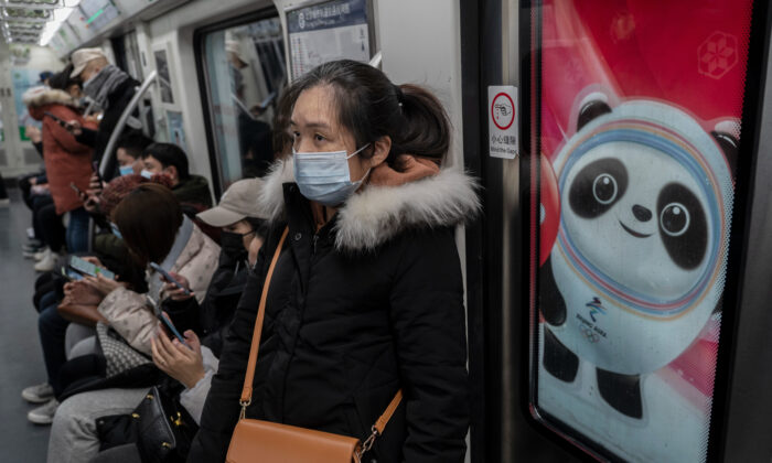 A woman people ride on a metro car next to a logo for Beijing 2022 Winter Olympics mascot Bing Dwen Dwen during rush hour in Beijing on Jan. 13, 2022. (Kevin Frayer/Getty Images)
