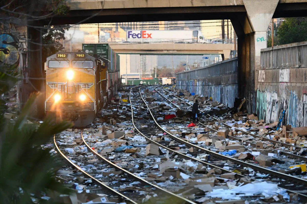 A person carries items collected from the train tracks as a Union Pacific locomotive passes through a section of Union Pacific train tracks littered with thousands of opened boxes and packages stolen from cargo shipping containers, targeted by thieves as the trains stop in downtown Los Angeles, Calif., on Jan. 14, 2022. (Patrick T. Fallon/AFP via Getty Images)