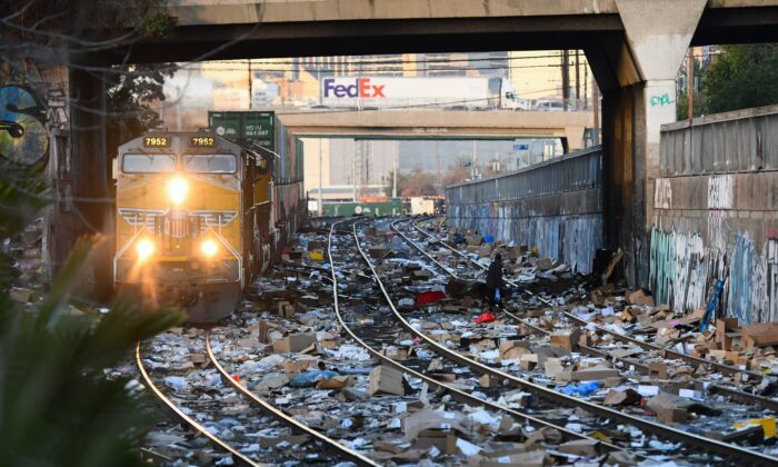 A person carries items collected from the train tracks as a Union Pacific locomotive passes through a section of Union Pacific train tracks littered with thousands of opened boxes and packages stolen from cargo shipping containers, targeted by thieves as the trains stop in downtown Los Angeles, Calif., on Jan. 14, 2022. (Patrick T. Fallon/AFP via Getty Images)