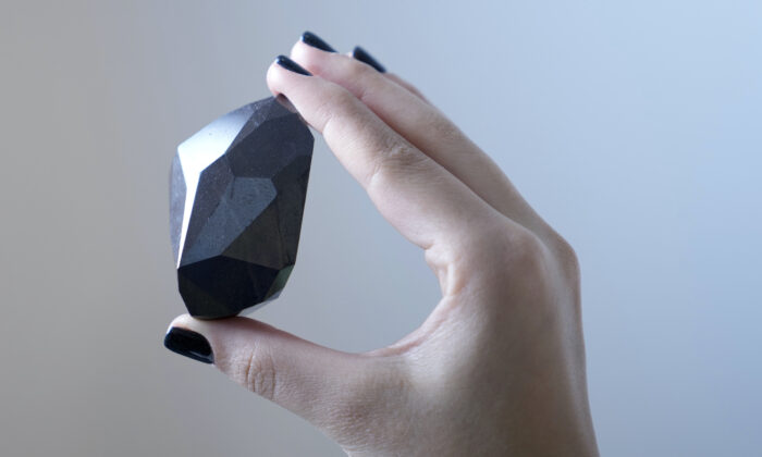 An employee of Sotheby's Dubai presents a 555.55 Carat Black Diamond “The Enigma” during the World Unveiling of Major auction highlight at Sotheby's Dubai gallery, in Dubai, United Arab Emirates, on Jan. 17, 2022. (Kamran Jebreili/AP Photo)