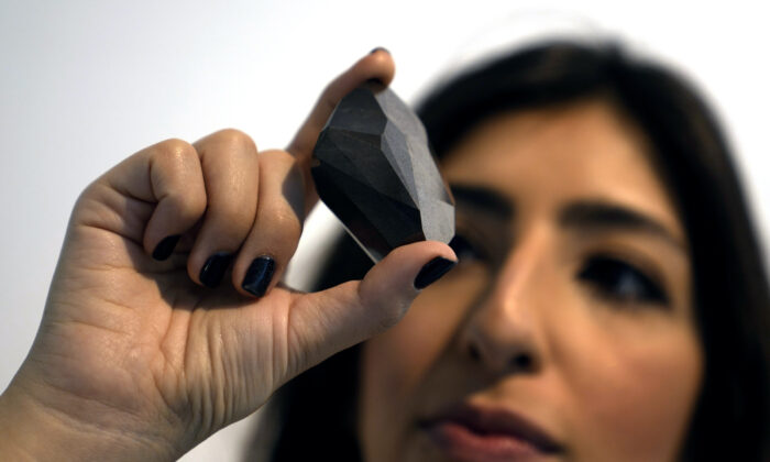 An employee of Sotheby's Dubai presents a 555.55 Carat Black Diamond, “The Enigma,” during the World Unveiling of Major auction highlight at Sotheby's Dubai gallery, in Dubai, United Arab Emirates, on Jan. 17, 2022. (Kamran Jebreili/AP Photo)