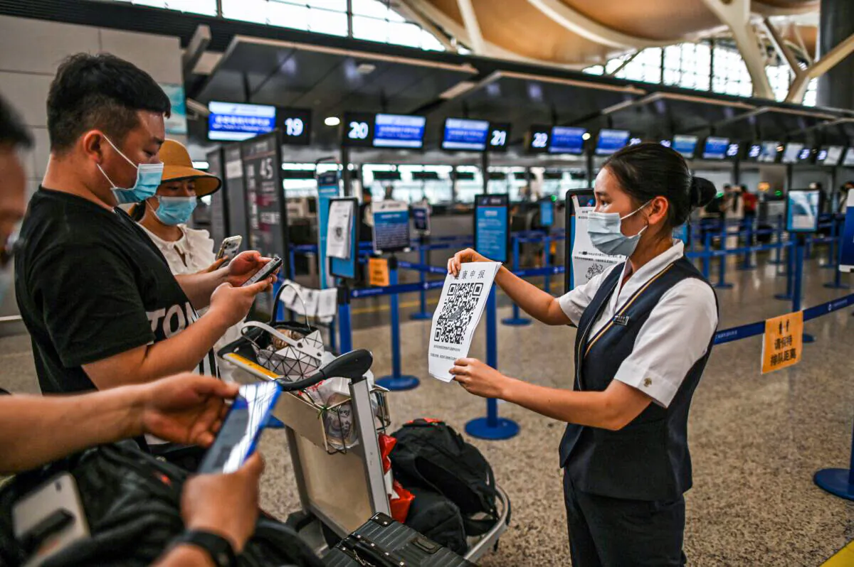 Passengers wearing facemasks check their health code with a sheet held by an aiport staff (R) before the counter area following preventive procedures against the spread of the COVID-19 coronavirus in Pudong International Airport in Shanghai, on June 11, 2020. (Hector Retamal/AFP via Getty Images)