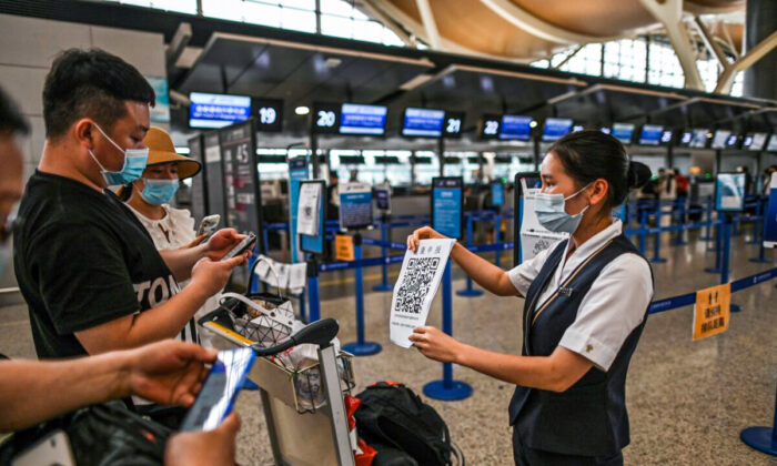 Passengers wearing facemasks check their health code with a sheet held by an aiport staff (R) before the counter area following preventive procedures against the spread of the COVID-19 coronavirus in Pudong International Airport in Shanghai, on June 11, 2020. (Hector Retamal/AFP via Getty Images)