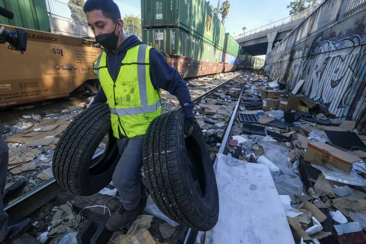 Contractor worker Luis Rosas removes vehicle tires from the shredded boxes and packages along a section of the Union Pacific train tracks in downtown Los Angeles, on Jan. 14, 2022. (Ringo H.W. Chiu/AP Photo)