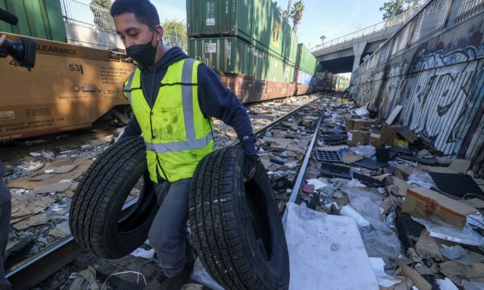 Contractor worker Luis Rosas removes vehicle tires from the shredded boxes and packages along a section of the Union Pacific train tracks in downtown Los Angeles, on Jan. 14, 2022. (Ringo H.W. Chiu/AP Photo)