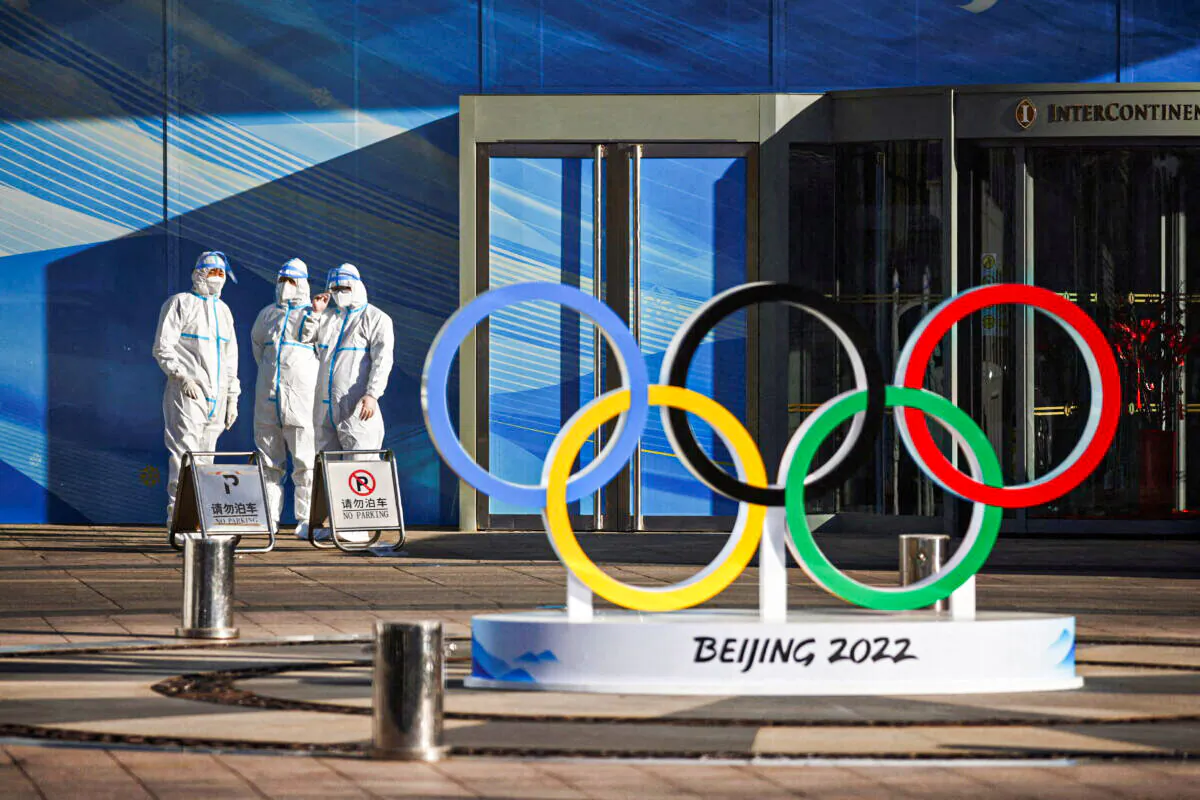 Workers in PPE stand next to the Olympic rings inside the closed loop area near the National Stadium, or the Bird's Nest, where the opening and closing ceremonies of Beijing 2022 Winter Olympics will be held, in Beijing, China, on Dec. 30, 2021. (Thomas Peter/Reuters)