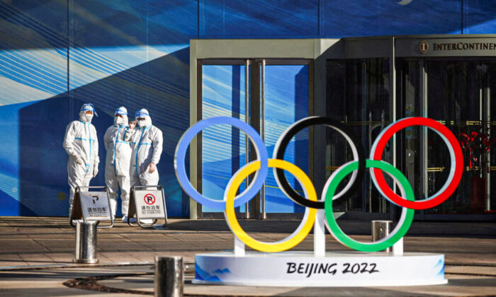 Workers in PPE stand next to the Olympic rings inside the closed loop area near the National Stadium, or the Bird's Nest, where the opening and closing ceremonies of Beijing 2022 Winter Olympics will be held, in Beijing, China, on Dec. 30, 2021. (Thomas Peter/Reuters)
