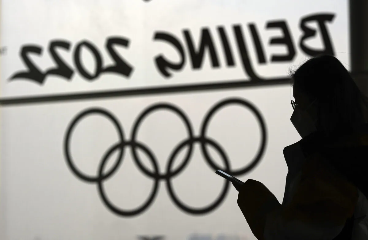 A woman looks at her phone as she passes an Olympic logo inside the main media centre for the Beijing Winter Olympics in Beijing on on Jan. 18, 2022. (David J. Phillip/AP Photo)