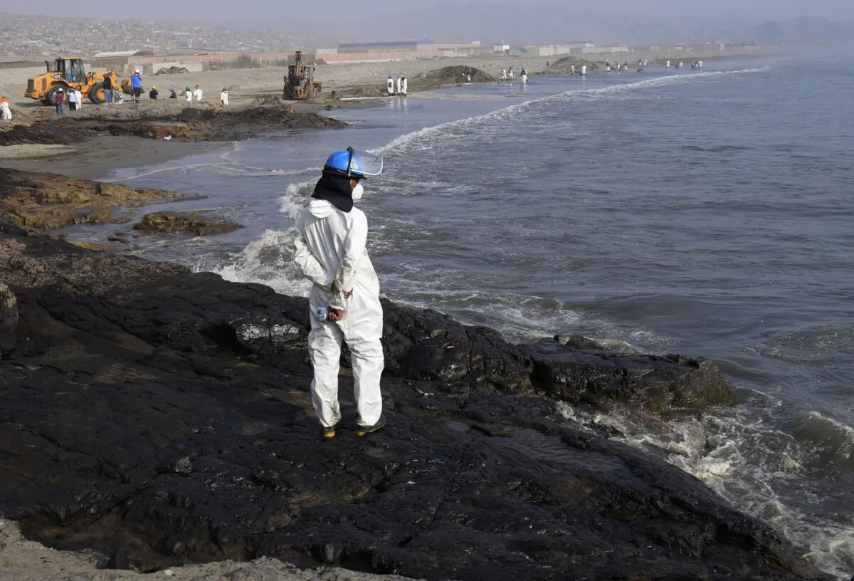 A workers stand on a rock covered with oil as other help with the clean up at Cavero beach in Ventanilla, Callao, Peru, on Jan. 17, 2022. (Martin Mejia/AP Photo)