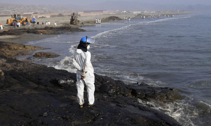 A workers stand on a rock covered with oil as other help with the clean up at Cavero beach in Ventanilla, Callao, Peru, on Jan. 17, 2022. (Martin Mejia/AP Photo)