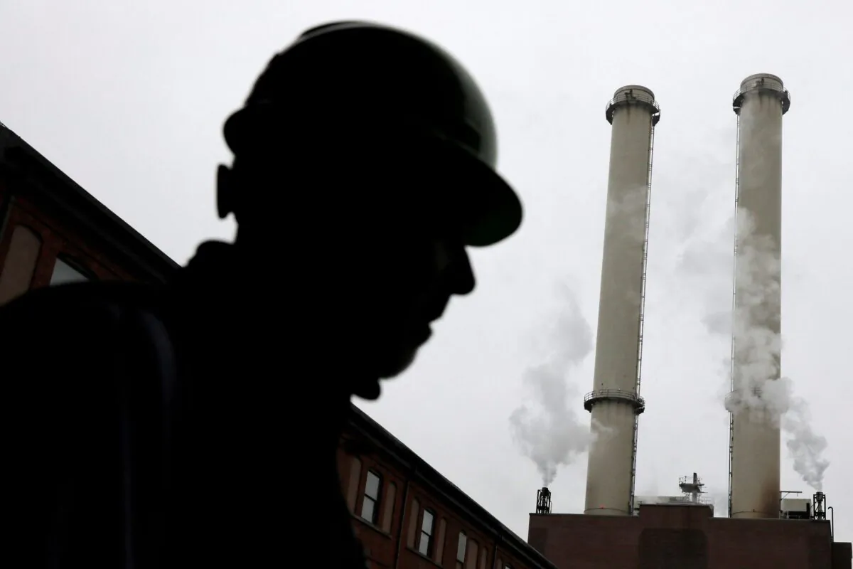 A worker stands near the chimney stacks of a neighboring factory at IceStone, a manufacturer of recycled glass countertops and surfaces, in New York City, N.Y., on June 3, 2021. (Andrew Kelly/Reuters)