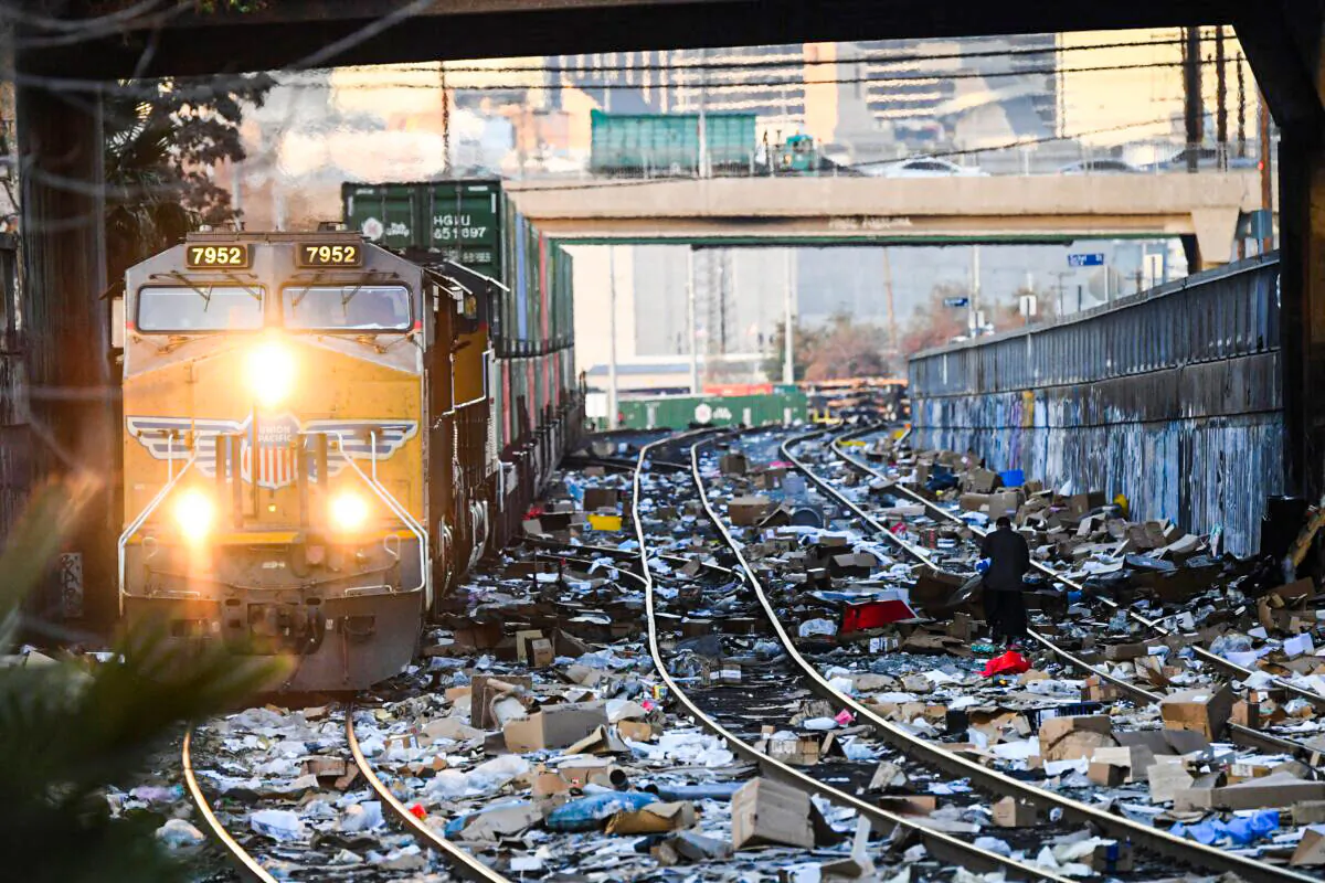 A person carries items collected from the train tracks as a Union Pacific locomotive passes through a section of Union Pacific train tracks littered with thousands of opened boxes and packages stolen from cargo shipping containers targeted by thieves as the trains stop in downtown Los Angeles on Jan. 14, 2022. (Patrick T. Fallon/AFP via Getty Images)