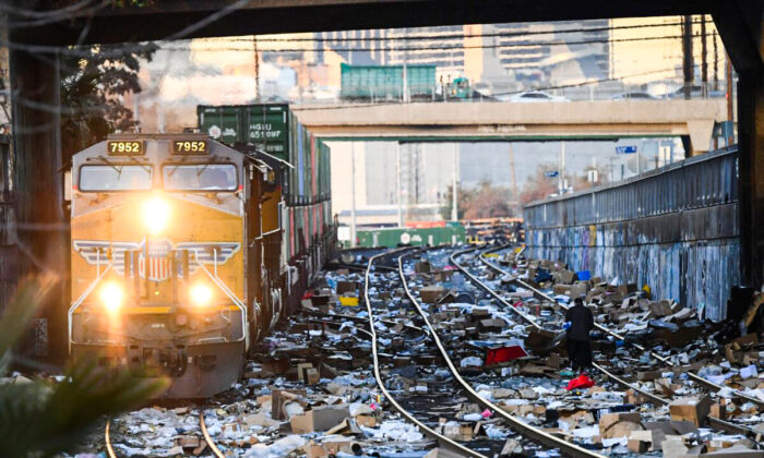 A person carries items collected from the train tracks as a Union Pacific locomotive passes through a section of Union Pacific train tracks littered with thousands of opened boxes and packages stolen from cargo shipping containers targeted by thieves as the trains stop in downtown Los Angeles on Jan. 14, 2022. (Patrick T. Fallon/AFP via Getty Images)