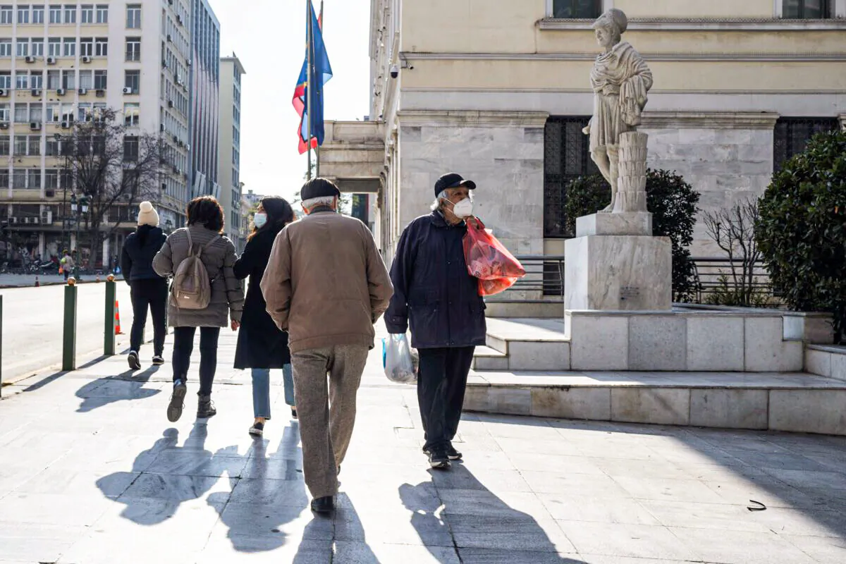 An elderly man wearing a face mask to curb the spread of coronavirus, walks past Athens' municipality building and in front of the statue of the ancient statesman Pericles of Athens' Golden Age, on Jan. 17, 2022. (Petros Giannakouris/AP Photo)