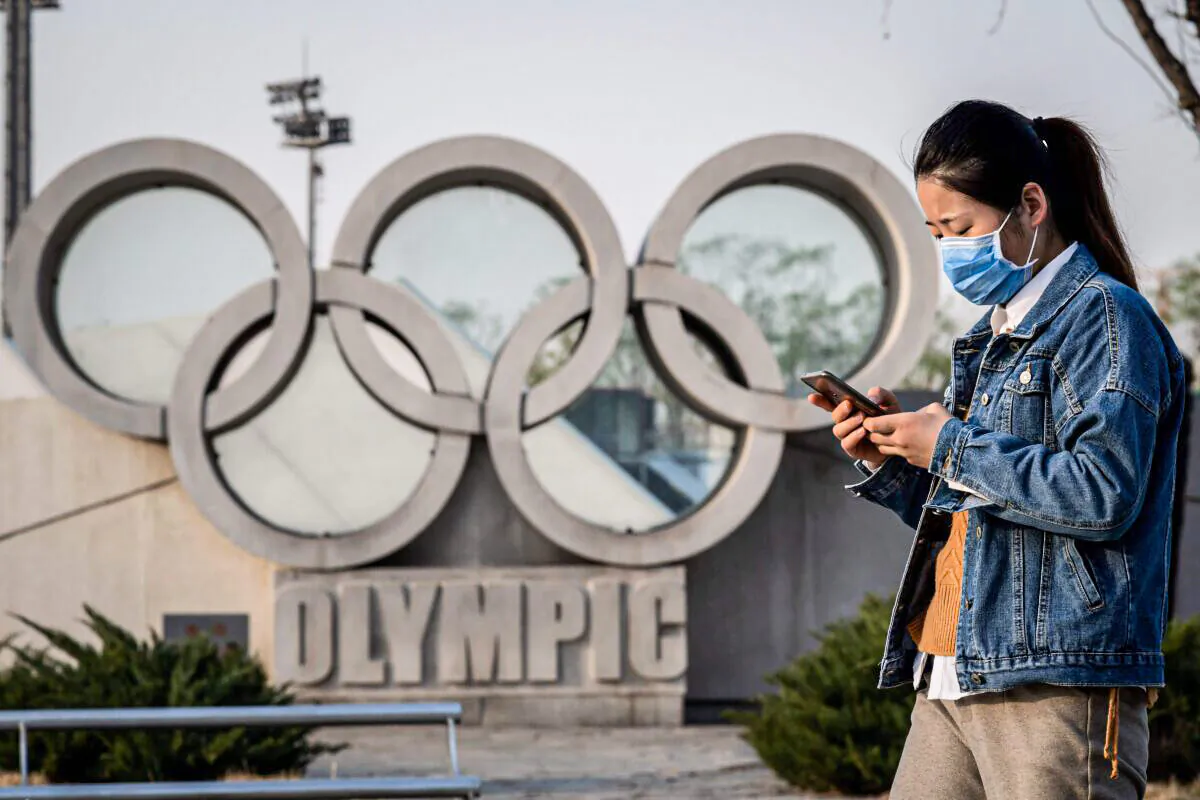 A woman wearing a mask walks before an Olympic rings sculpture at the national “Birds Nest” stadium in Beijing on March 23, 2020. (Nicolas Asfouri/AFP via Getty Images)