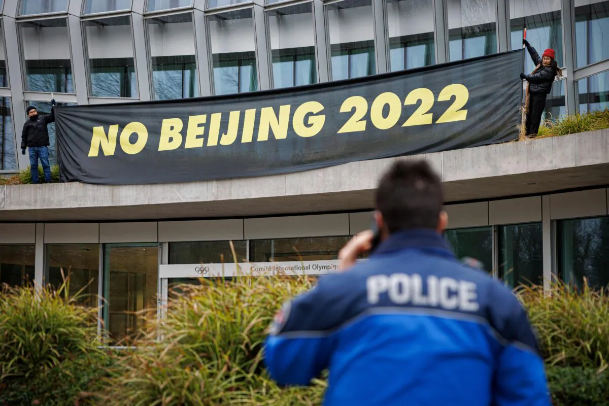 A policeman talks on the phone as Tibetan activists from the Students for a Free Tibet association hang a banner during a protest in front of the International Olympic Committee (IOC) headquarters ahead of February's Beijing 2022 Winter Olympics, in Lausanne, on Dec. 11, 2021. (Valentin Flauraud/AFP via Getty Images)