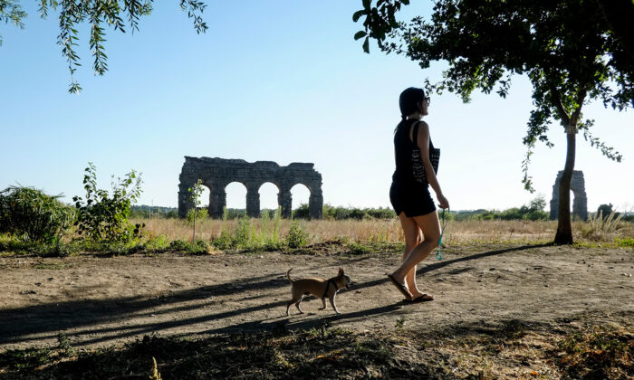 A woman walks a dog near the ruins of an ancient Roman aqueduct, in a park in a suburb of Rome on July 28, 2017. (Andreas Solaro/AFP via Getty Images)