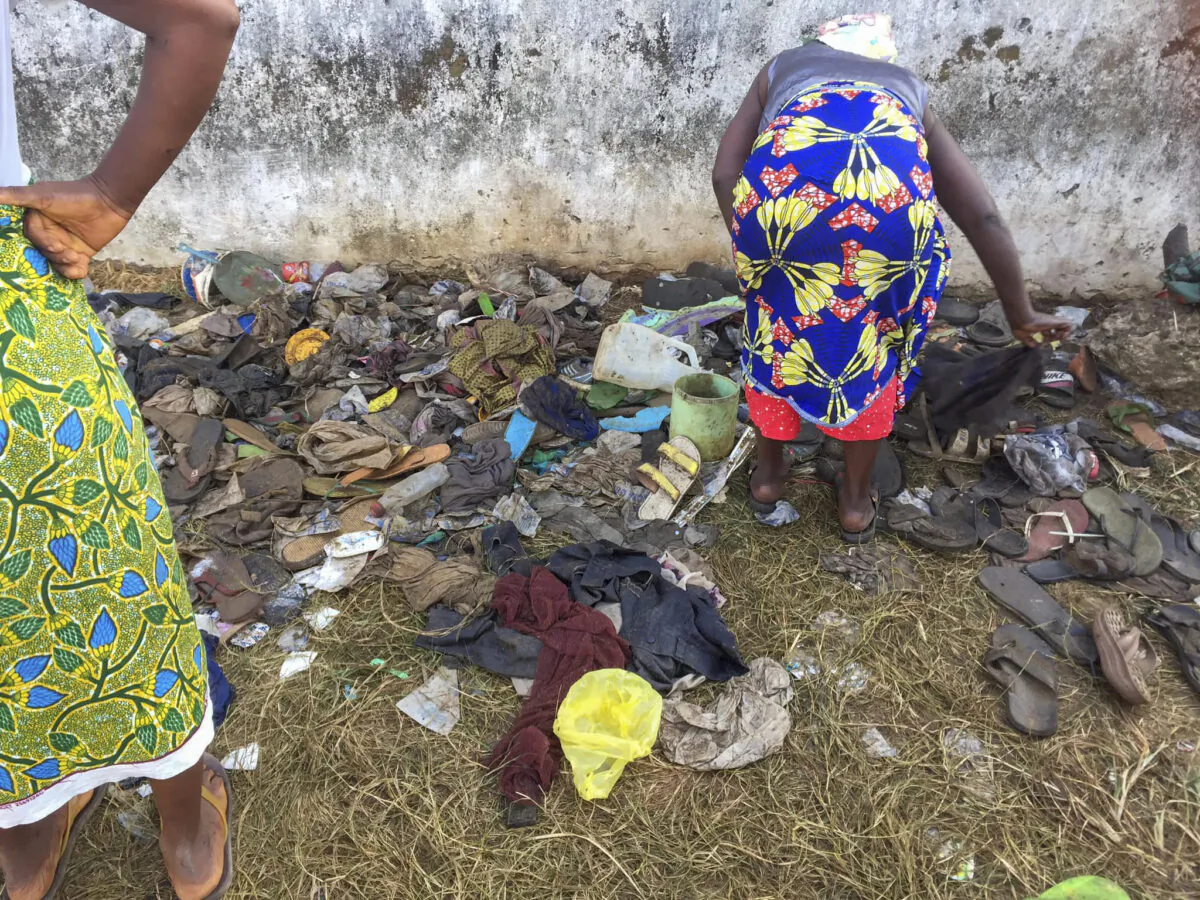 A woman searching through shoes at the entrance of a field where 29 persons, including 11 children and a pregnant woman have been confirmed killed after they were trampled upon in a stampede at a Christian crusade in New Kru Town, outside Monrovia, Liberia on Jan. 20, 2022. (Augustine D Wallace via AP)