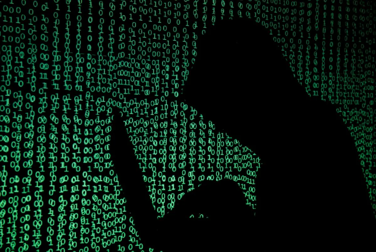 A hooded man holds a laptop computer as cyber code is projected onto him in this illustration picture taken on May 13, 2017. (Kacper Pempel/Reuters)