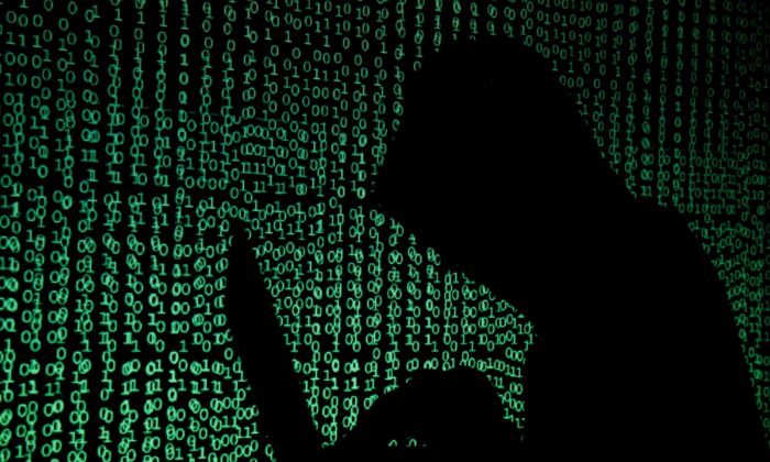 A hooded man holds a laptop computer as cyber code is projected onto him in this illustration picture taken on May 13, 2017. (Kacper Pempel/Reuters)