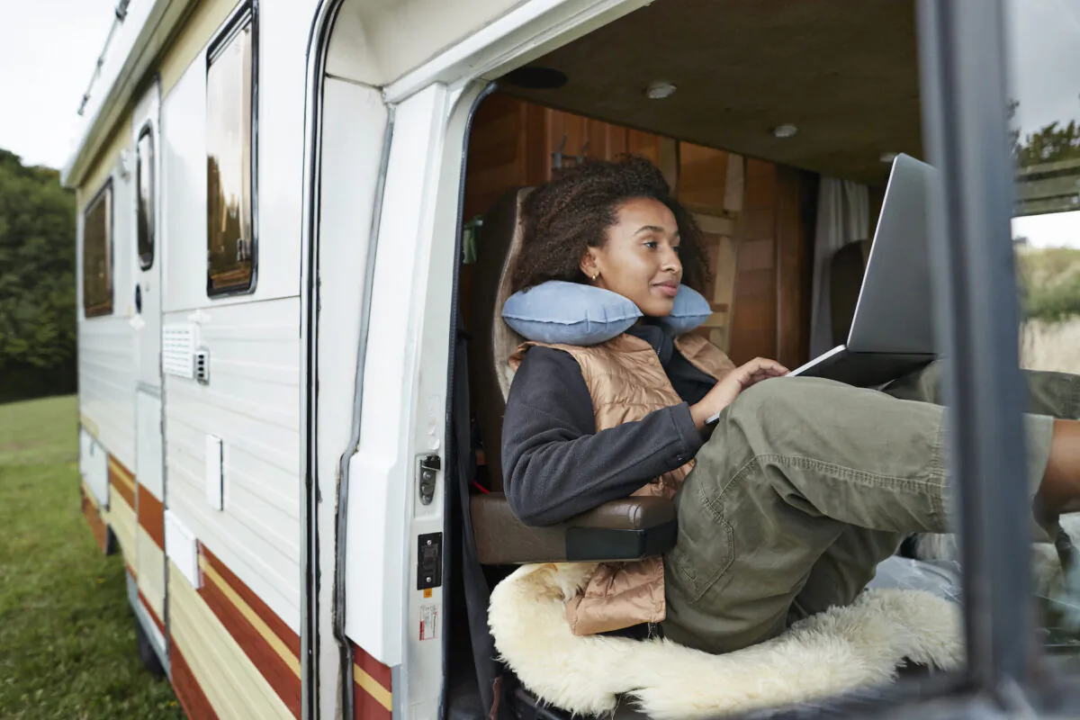 Young woman with a neck pillow using a laptop in a motor van. (Klaus Vedfelt/Getty Image)