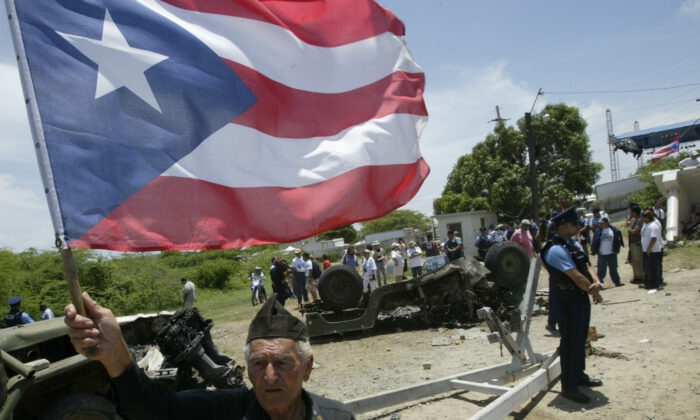 Bernardo Rivera celebrates holding a Puerto Rican Flag as he walks around a burned military vehicle at the former U.S. Naval Station Camp Garcia in Vieques, Puerto Rico, on May 1, 2003. The U.S. Navy abandoned Camp Garcia just before midnight on April 30 with a ceremony marking the land transfer back to Puerto Rico. Hundreds of protesters then rushed onto the former Navy area, destroying vehicles, burning flags and attacking buildings. Vieques served as a practice bombing range for U.S. Navy for almost 60 years. (Gerald Lopez-Cepero/Getty Images)