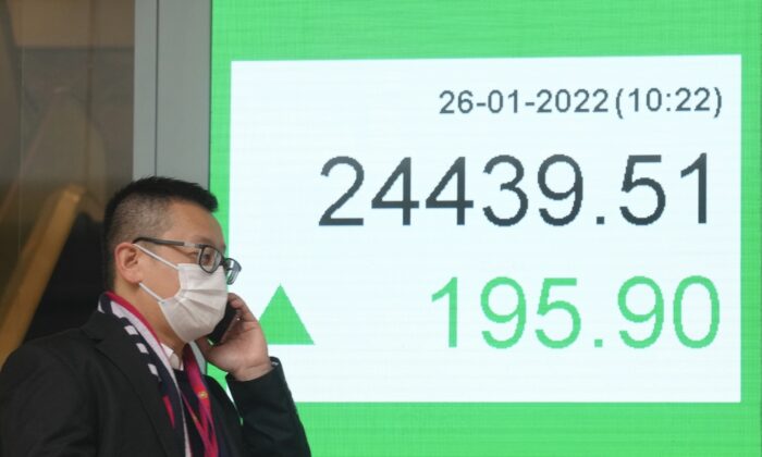 A man wearing a face mask walks past a bank's electronic board showing the Hong Kong share index in Hong Kong, on Jan. 26, 2022. (Kin Cheung/AP Photo)