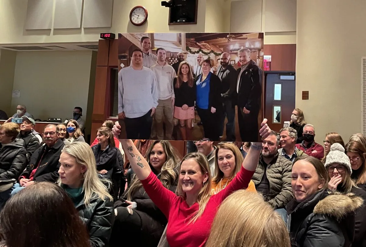 An attendee holds up a board member group photo in which they were all unmasked during the Loudoun County school board meeting in Ashburn, Va., on Jan. 25, 2022. (Terri Wu/The Epoch Times)