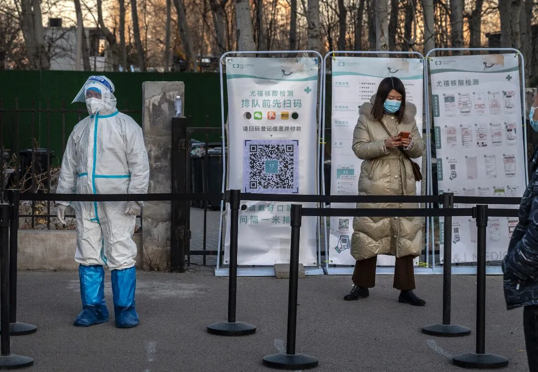 A medical worker stands in protective equipment as a client registers for a nucleic acid test at a private outdoor clinic in Beijing, China, on Dec. 27, 2021. (Kevin Frayer/Getty Images)