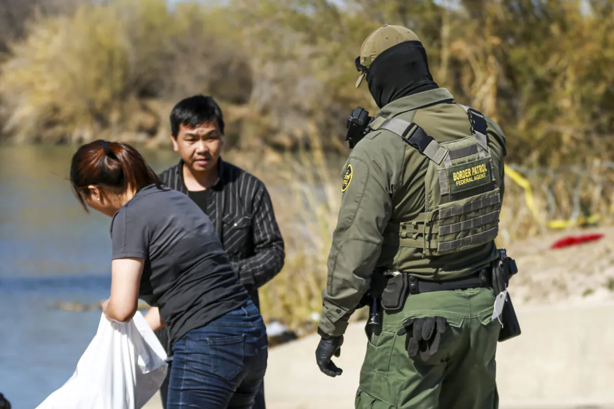 A Border Patrol agent apprehends a Chinese couple that just waded across the Rio Grande from Mexico into Eagle Pass, Texas, on Jan. 25, 2022. (Charlotte Cuthbertson/The Epoch Times)