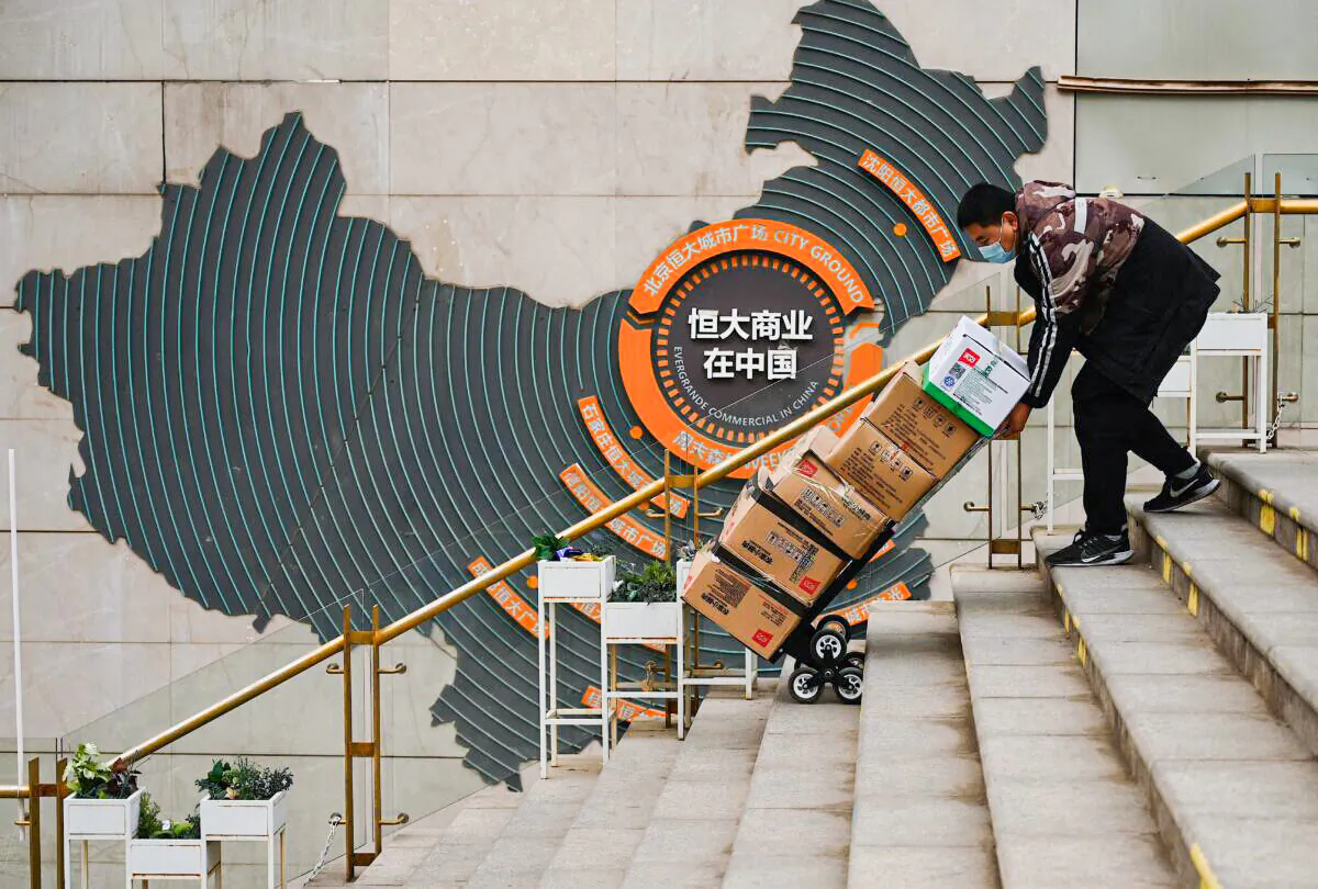 A worker pushes a cart in front of a sign showing Evergrande Group's China operation at a housing complex by the property developer in Beijing on Dec. 8, 2021. (Noel Celis/AFP via Getty Images)