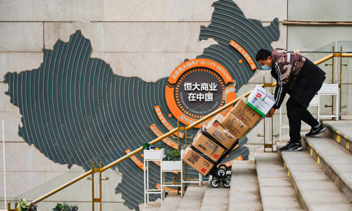 A worker pushes a cart in front of a sign showing Evergrande Group's China operation at a housing complex by the property developer in Beijing on Dec. 8, 2021. (Noel Celis/AFP via Getty Images)