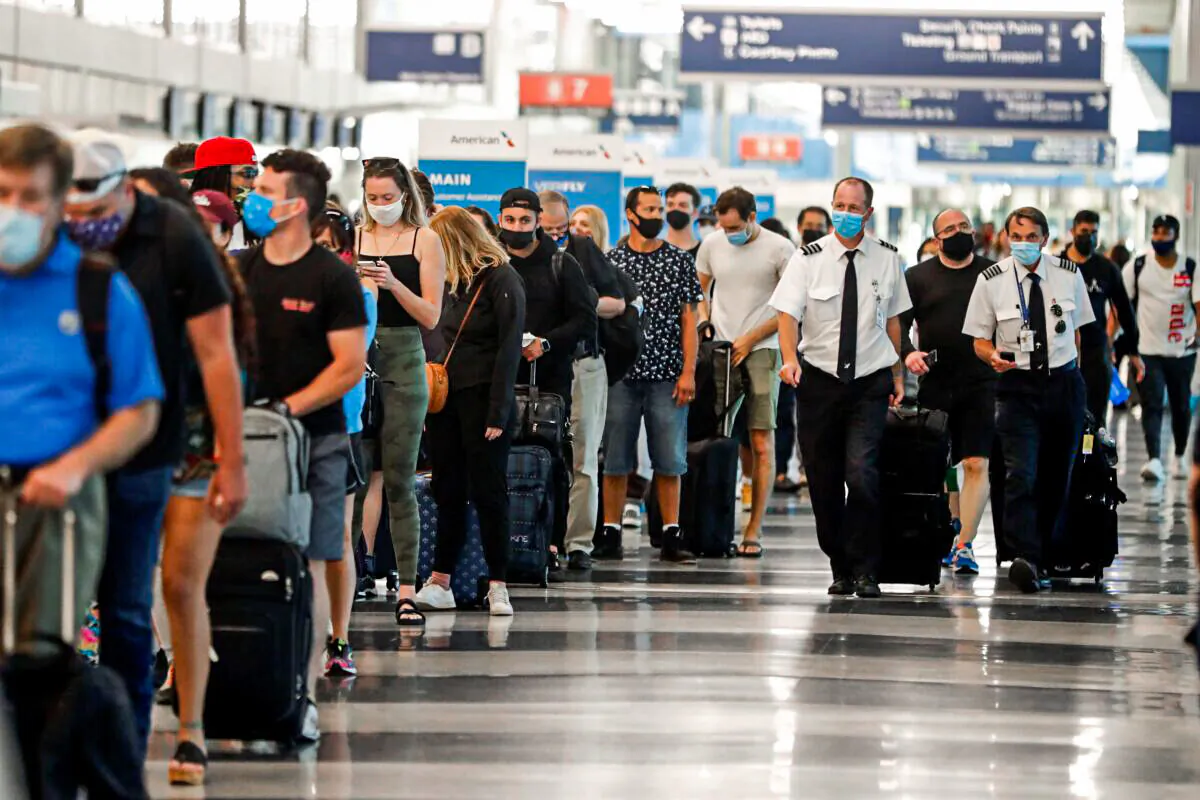 Two airplane pilots pass by a line of passengers while waiting at a security check-in line at O'Hare International Airport in Chicago, Ill., on July 1, 2021. (Shafkat Anowar/AP Photo)