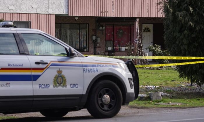 An RCMP officer sits outside a home surrounded by police tape where four people were found dead Tuesday, in Richmond, B.C., on Jan. 26, 2022. (The Canadian Press/Darryl Dyck)