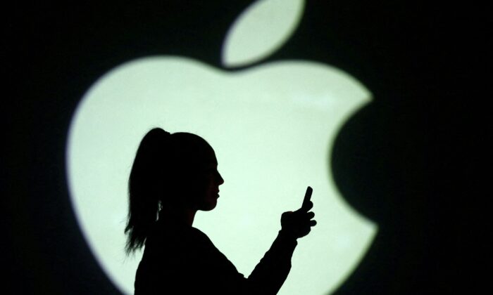 Silhouette of mobile user is seen next to a screen projection of Apple logo in this picture illustration taken, on March 28, 2018. (Dado Ruvic/Reuters, Illustration)