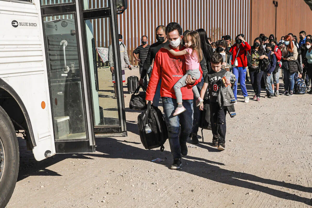 Illegal immigrants who have gathered by the border wall prepare to board a bus going to to the Border Patrol station for processing in Yuma, Ariz., on Dec. 10 2021. (Charlotte Cuthbertson/The Epoch Times)