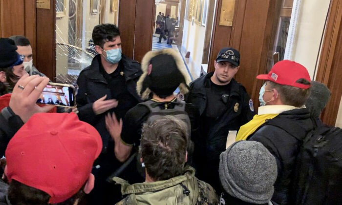 Christopher Ray Grider (at right with yellow flag tied around his neck) just before he hands a black helmet to rioter Zachary Alam at the Speaker's Lobby on Jan. 6, 2021. (Video Still/Sam Montoya for The Epoch Times)