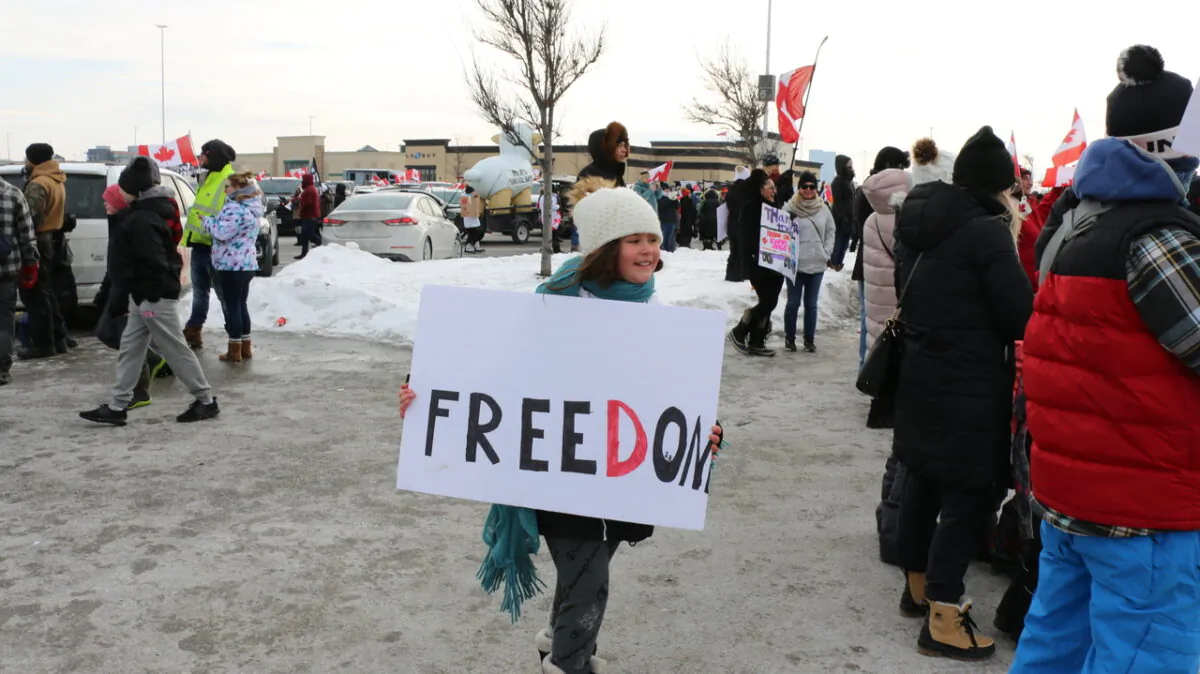 A child was seen holding a sign that reads "Freedom," at Vaughan Mills, northwest of Toronto, Ontario, on Jan. 27, 2022. Several thousands of supporters came out to cheer on the "Freedom Convoy 2022" that passed through the city en route to Ottawa. (Andrew Chen/The Epoch Times)