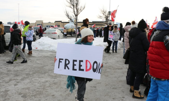 A child was seen holding a sign that reads "Freedom," at Vaughan Mills, northwest of Toronto, Ontario, on Jan. 27, 2022. Several thousands of supporters came out to cheer on the "Freedom Convoy 2022" that passed through the city en route to Ottawa. (Andrew Chen/The Epoch Times)