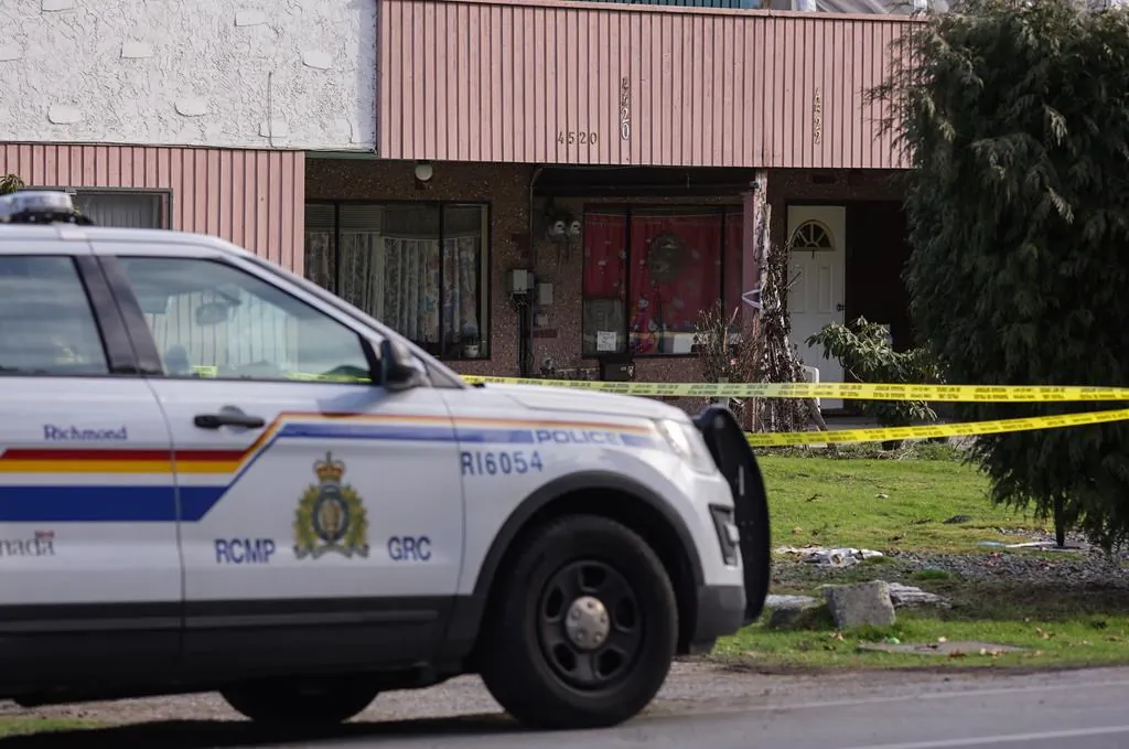 An RCMP officer sits outside a home surrounded by police tape in Richmond, B.C., on Jan. 26, 2022. (The Canadian Press/Darryl Dyck)