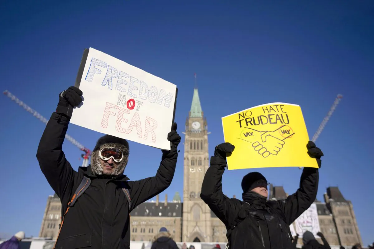 Protesters participating in a cross-country truck convoy protesting vaccine mandates and other restrictions hold signs on Parliament Hill in Ottawa on Jan. 29, 2022. (The Canadian Press/Adrian Wyld)
